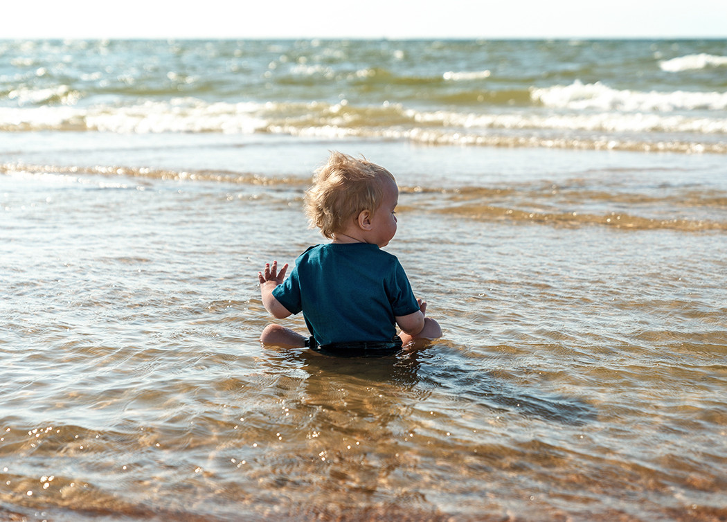 Baby sitzt am Strand im Wasser der Ostsee